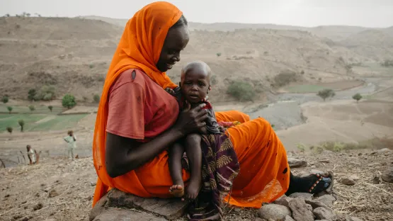 Eine geflüchtete Mutter in Darfur schützt ihr Baby mit einem Schal.